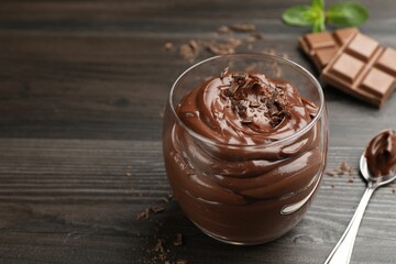 Delicious chocolate pudding in glass and spoon on wooden table, closeup. Space for text