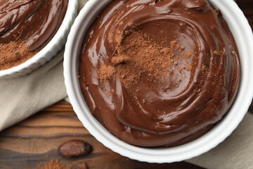 Tasty chocolate pudding in bowls and cocoa beans on wooden table, flat lay