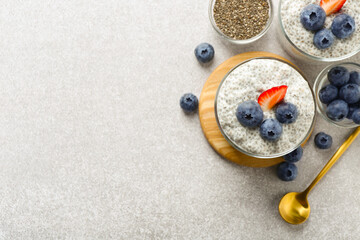 Superfood. Delicious pudding with chia seeds, yogurt, blueberries, granola and strawberry on light grey table, flat lay. Space for text