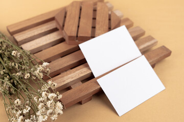 White blank business card mockup with wooden decoration and dried flower on brown background