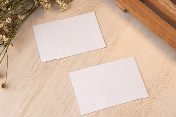 White blank business card mockup with wooden decoration and dried flower on brown background