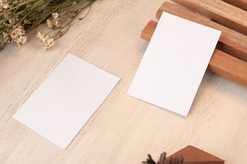 White blank business card mockup with wooden decoration and dried flower on brown background