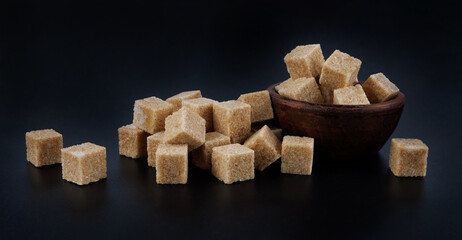 Clay cup with brown sugar cubes on black background. Cane brown sugar.