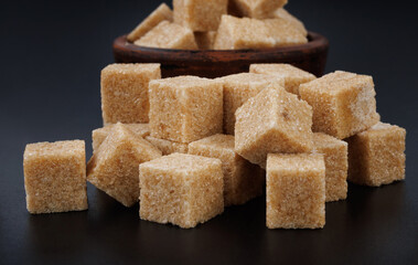 Clay cup with sugar cubes on black background. Cane brown sugar.