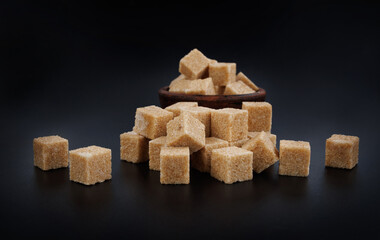 Clay cup with sugar cubes on black background, side view. Cane brown sugar.