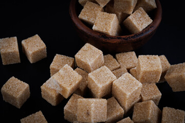 Clay cup with sugar cubes on black background, top view. Cane brown sugar.