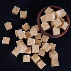Clay cup with sugar cubes on black background, top view. Cane brown sugar.