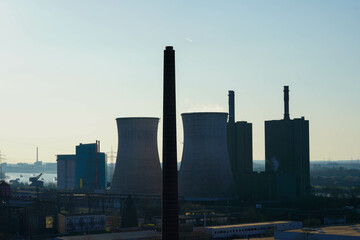 A power plant with large cooling towers and chimneys is seen against the evening sky