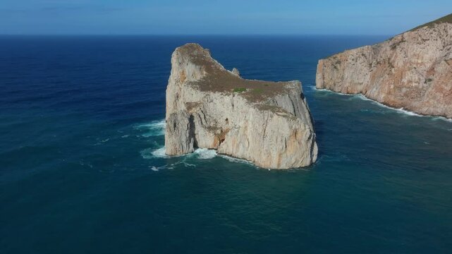 Orbiting drone shot of Pan di Zucchero rising from the Mediterranean Sea near Masua, Sardinia isolated limestone stack contrasting with the calm sea and the rugged cliffs of the surrounding coast.