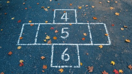 A fall-themed hopscotch with numbers for children to play on. The ground is adorned with autumn leaves and the outdoor play is enhanced by this seasonal decoration.