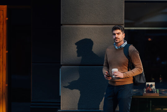Businessman drinking coffee and using smartphone in urban setting