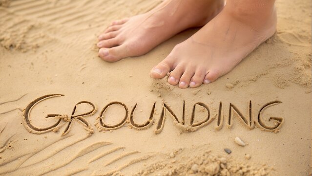 "Close-up flat lay of bare feet on sand with 'Grounding' written in front, mindfulness beach walk or earthing therapy concept"

