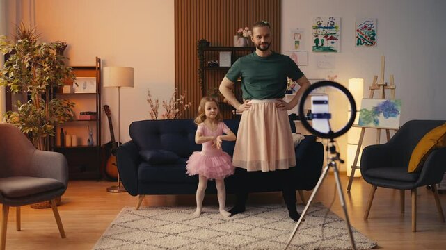 Cute little girl and her dad in tutu skirts recording dance video on smartphone