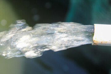 Close-up of water gushing from a white pipe, captured mid-motion with sunlight highlighting the...