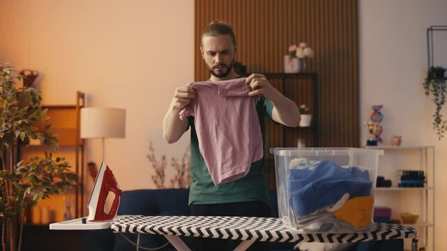 Upset young man looking at clothes shrunk after washing, laundry chore fail