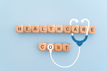 HEALTHCARE COST text on wooden cube block with stethoscope icon and blue background, for health...