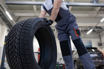 Unrecognizable automotive technician in garage checking wheel and fixing tire ensuring vehicle safety