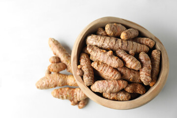 Raw turmeric roots in bowl on white marble table, closeup