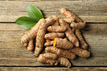 Pile of tumeric rhizomes with leaves on wooden table, top view