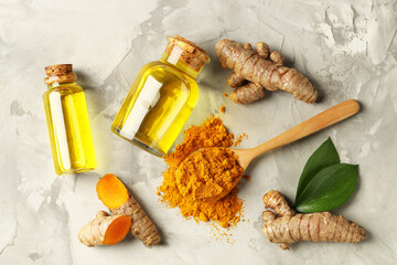 Turmeric oil, roots, powder and green leaves on grey textured table, flat lay