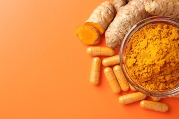Turmeric powder in bowl, roots and capsules on orange background, flat lay. Space for text