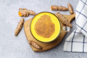 Tasty turmeric latte in cup and roots on grey table, flat lay