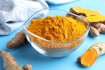 Aromatic turmeric powder in bowl and fresh roots on light blue wooden table, closeup