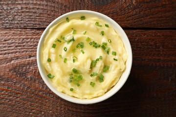 Tasty mashed potato with green onion in bowl on wooden table, top view