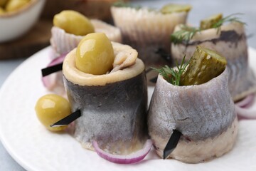 Delicious herring rolls with olives, pickles, dill and onion on table, closeup