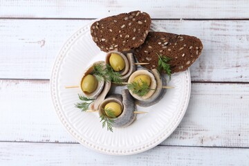 Delicious herring rolls with olives, dill and bread on white wooden table, top view