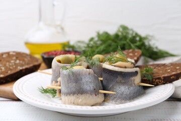 Delicious herring rolls with olives, dill and bread on white wooden table, closeup