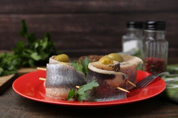 Delicious herring rolls with olives and parsley on wooden table, closeup