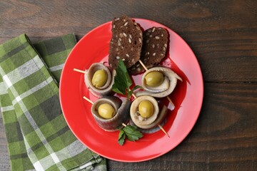 Delicious herring rolls with olives, parsley and bread on wooden table, top view