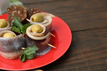 Delicious herring rolls with olives, parsley and bread on wooden table, closeup. Space for text