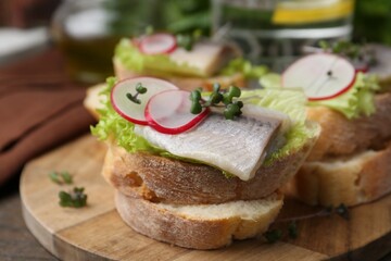 Tasty sandwiches with herring, radish and lettuce on table, closeup