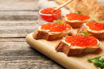 Sandwiches with red caviar and microgreens on wooden table, closeup