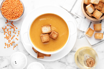 Delicious lentil cream soup served with croutons on white marble table, flat lay