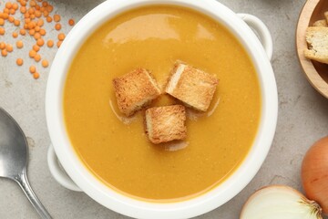 Delicious lentil cream soup served with croutons on light grey table, flat lay