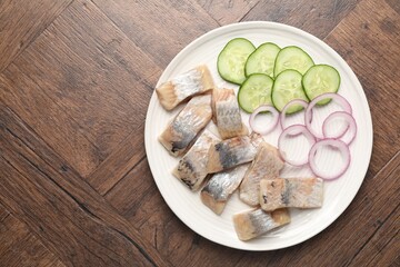 Pieces of delicious herring, onions and cucumber slices on wooden table, top view. Space for text