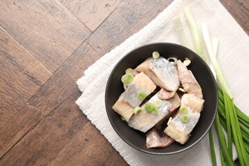 Pieces of delicious herring with green onions on wooden table, top view. Space for text