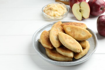 Delicious fried pyrizhky (stuffed pies) and apples on white wooden table, closeup. Space for text