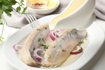 Pouring oil on tasty herring fillets with onions and parsley at table, closeup