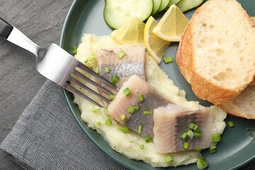 Pieces of delicious herring, mashed potato, cucumber slices and bread served on black table, closeup