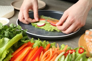Woman making tasty spring roll at grey wooden table, closeup