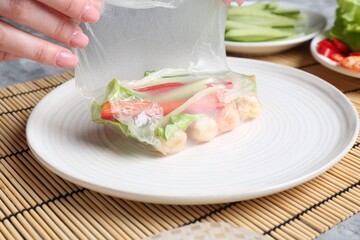 Woman making tasty spring roll at light grey table, closeup