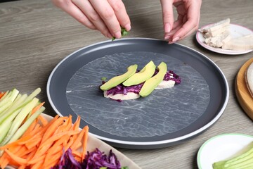 Woman making tasty spring roll at grey wooden table, closeup