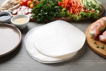 Rice paper sheets and different ingredients on grey wooden table, closeup