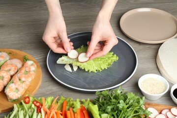 Woman making tasty spring roll at grey wooden table, closeup