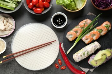 Rice paper sheets and different ingredients on dark grey table, flat lay