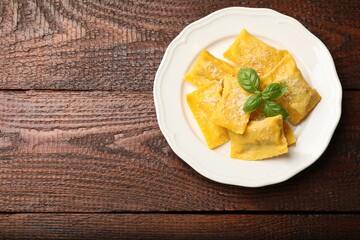 Delicious ravioli with parmesan cheese and basil on wooden table, top view. Space for text